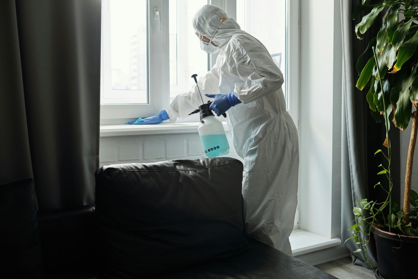Técnico con equipo de protección completo descontaminando una ventana